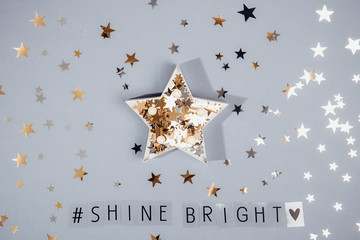 Top view hashtag Shine bright phrase and star shape full of glittering stars confetti on the grey background with shining stars. Everyday Inspirational quotes concept. Be unique. Selective focus.