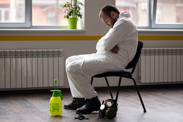 Tired of working day disinfector in a protective suit and mask. Resting after work. The fight against coronovirus.