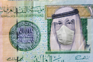 COVID-19 coronavirus in Gulf, 1 Riyal money bill with face mask. Coronavirus affects global stock market. World economy hit by corona virus outbreak and pandemic fears. Crisis and finance concept.