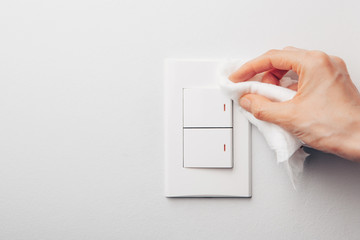 Close up view of woman hand using antibacterial wet wipe for disinfecting home room electric switch on grey wall
