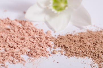 Cosmetic beige powder in different shades on a white background with a flower.