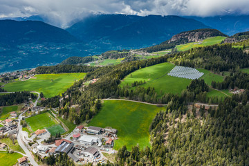 Aerial view of farm of solar batteries on green slopes of the mountains of Italy, Trentino, huge clouds over a valley, roofs of houses of settlements, green meadows, a clear energy, energy of the sun