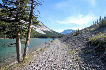 Rocky hiking trail along a river at the base of a mountain.