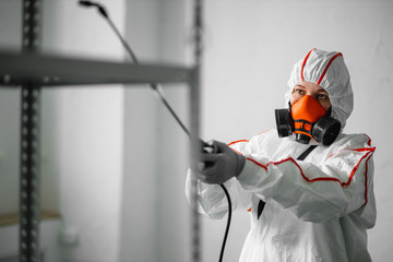 professional disinfector in an NBC personal protective equipment ppe suit, gloves, mask, cleaning...
