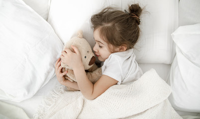 A cute little girl is sleeping in a bed with a Teddy bear toy .