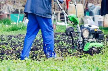 A man plows the land with a cultivator in a spring garden