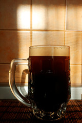 transparent glass half-liter mug with dark beer with foam in the sunlight