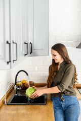 A woman washes cabbage under running water