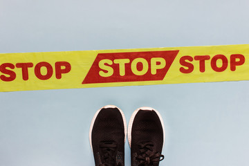 Quarantine forbidding Stop tape and sneakers shoes on blue background.