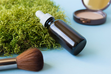 Mockup template of dark glass bottle with pipette, bristle brush, bronzer laying on green moss.