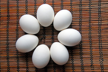 seven fresh white chicken eggs lying on a bamboo napkin