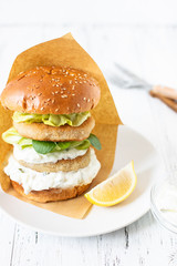 Delicious healthy crispy fish burger with greek yogurt-based sauce with lettuce and cucumber. White background, close-up, selective focus, copy-space