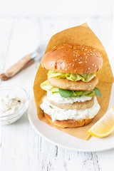 Delicious healthy crispy fish burger with greek yogurt-based sauce with lettuce and cucumber. White background, close-up, selective focus, copy-space