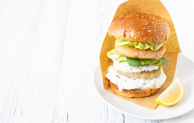 Delicious healthy crispy fish burger with greek yogurt-based sauce with lettuce and cucumber. White background, close-up, selective focus, copy-space