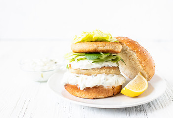 Delicious healthy crispy fish burger with greek yogurt-based sauce with lettuce and cucumber. White background, close-up, selective focus, copy-space