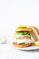Delicious healthy crispy fish burger with greek yogurt-based sauce with lettuce and cucumber. White background, close-up, selective focus, copy-space
