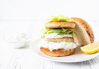 Delicious healthy crispy fish burger with greek yogurt-based sauce with lettuce and cucumber. White background, close-up, selective focus, copy-space