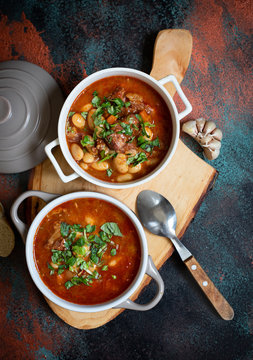 Bean soup with meat and vegetables served on a rustic board with garlic. Traditional Balkan soup or stew Corbast Pasulj (Grah). Top view, copy space