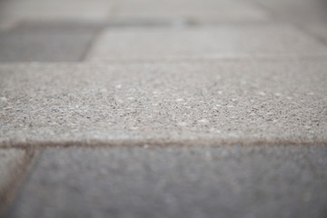 Narrow view of a concrete tile in the blurred sidewalk. Cement block on a pedestrian crossing. Textured abstract background bokeh.