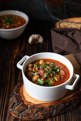 Bean soup with meat and vegetables served on a rustic board and wooden table with bread and garlic. Traditional Balkan soup Pasulj (Grah). Close-up, selective focus