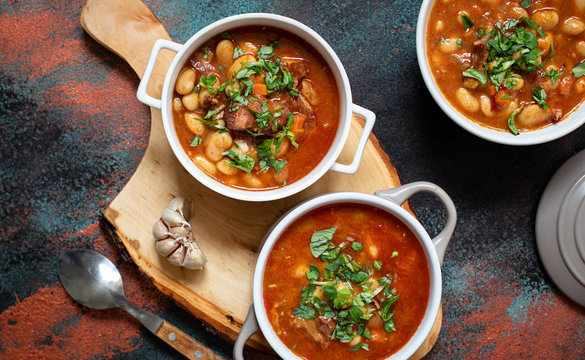Bean soup with meat and vegetables served on a rustic board with garlic. Traditional Balkan soup or stew Corbast Pasulj (Grah). Top view, copy space