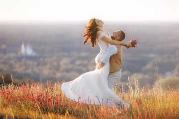 A loving groom circles the bride in his arms on the field in nature. Romantic portrait of the bride...