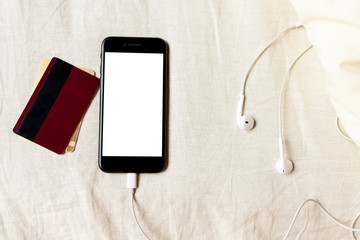 Smartphone with headphones and credit cards rumpled bed