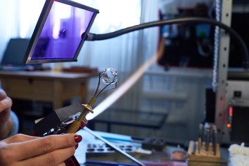 Young female artisan holding handtool with fixed small glass workpiece over fire