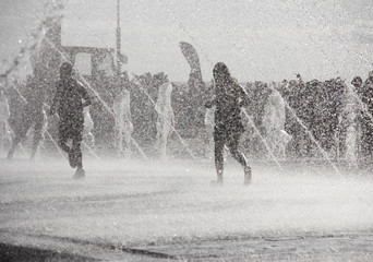 Silhouette of kids jumping in cool fountain water. A boy playing in water fountains. Happy children playing happily in the city fountain on a hot summer day