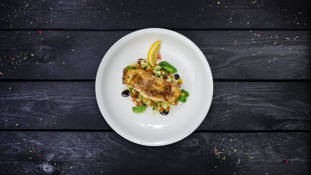 Baked cod fillet with vegetables rotating on white plate.