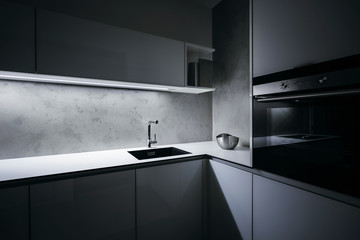 Modern white kitchen corner in minimalist design, during night, with light strip turned on, modern oven, granite sink, and premium materials such as glass, concrete, aluminum and stainless steel. - obrazy, fototapety, plakaty