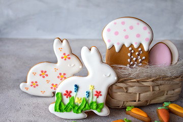 Easter cakes on a gray background and a wicker basket. Gingerbread in the form of a hare, carrot, egg and cake. Copy space. The concept of the Easter holiday and handmade. Banner, layout