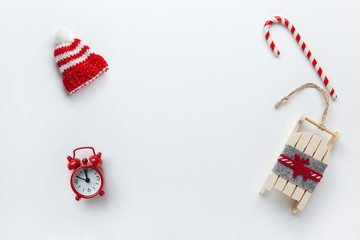 Fototapeta na wymiar Christmas flat lay, winter beanie hat, candy cane, small red analog clock, sled on white background, copy space. Minimal style. Top view. Celebration, festive, eco concept. Horizontal