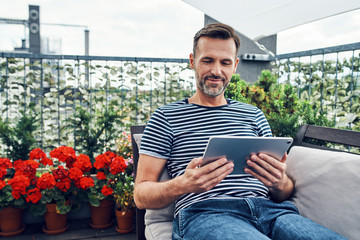 Adult man using digital tablet at apartment balcony - Powered by Adobe