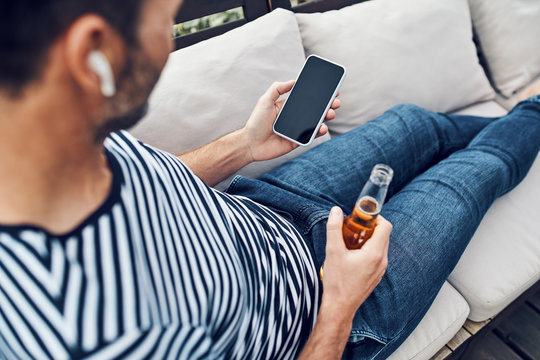 Close-up of man using smartphone while lounging on patio and drinking beer