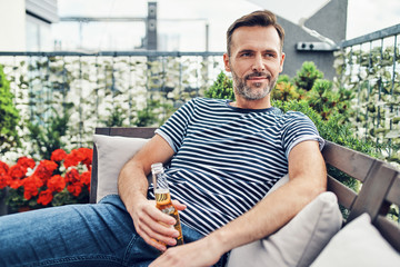 Smiling man sitting on terrace with beer and enjoying the sunny day
