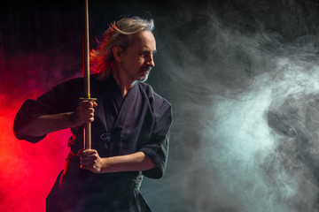 Fototapeta premium mature caucasian kendo fighter in suit with shinai bamboo sword , practicing fight before competitions. traditional japanese martial art concept. isolated colorful smoky space