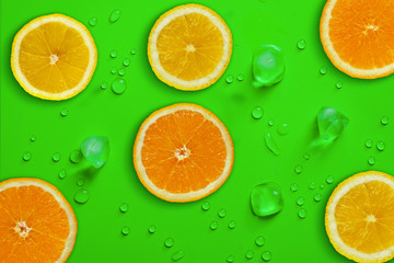 Fresh juicy slices of orange and lemon on bright green background covered with water drops