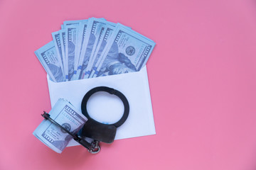 top view handcuffs on an envelope with money, pink background