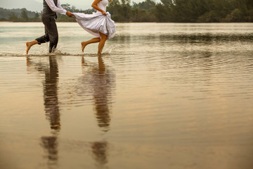 Noivos correndo no lago, com vestido de noiva e ele de roupa do casamento, brincando em casal. Traje de noiva para casamento na praia. - obrazy, fototapety, plakaty