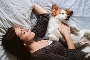 young woman and dog at home resting on bed. Love, togetherness and pets indoors