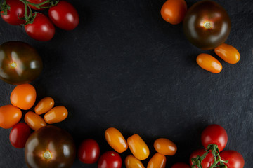 Different tomato feeds on a stone black background. Red on a branch, yellow, cherry, black tomatoes. Tomatoes close-up, top view.