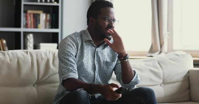 Emotional young african american guy watching disgusting tv program movie alone in living room, feeling confused shocked about horror film, violence in social media, awful news or morbid shows.