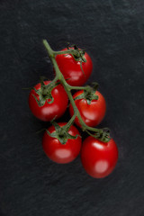 Different tomato feeds on a stone black background. Red on a branch, yellow, cherry, black tomatoes. Tomatoes close-up, top view.