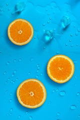 Fresh juicy slices of orange and ice cubes on the bright blue background covered with water drops