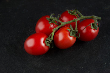 Different tomato feeds on a stone black background. Red on a branch, yellow, cherry, black tomatoes. Tomatoes close-up, top view.