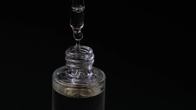 Women hand hold a glass bottle of iquid essential, collagen serum.with dropper on blurred background, close up. Black background