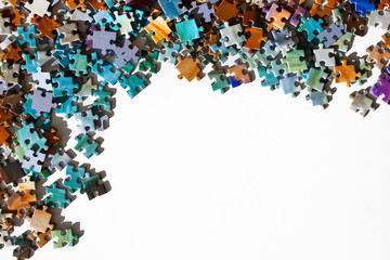 Top view of scattered multicolored jigsaw puzzle pieces. Lying on white table arranged as frame for copy space. Concept of putting together disconnected elements.