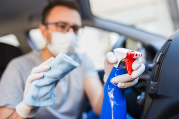 Man wearing medical mask and cleaning car air duct with microfiber cloth and spray bottle disinfectant.