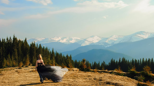 A woman walks in the mountains whose peaks are covered with snow